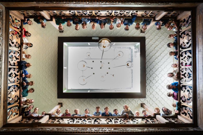 Boarding pupils smiling over the historic main building balcony at Old Buckenham Hall prep school in Suffolk.